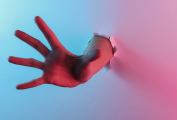 Mystical halloween concept. Hand through a torn hole. Creative pop art pink blue neon color. Trendy gradient illumination. Night light