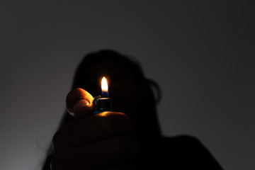 Woman holding a cork in front of her face and the cork flame lighting the scene.