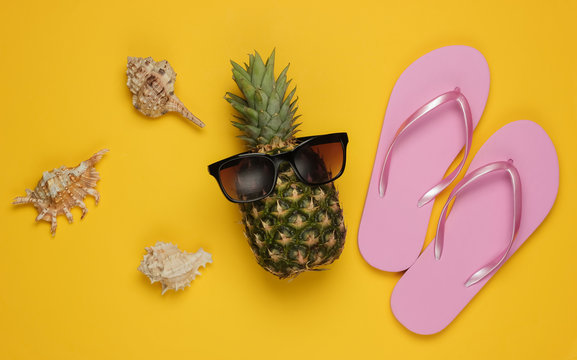 Summer background. Fun and humor. The concept of a beach holiday, travel. Pineapple with sunglasses, flip flops on yellow background. Top view