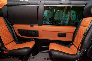 Four rear seats in a minibus are deployed to each other and tightened in black and brown leather with a diamond-shaped stitching thread in a workshop for tuning and repairing vehicles. Van car.
