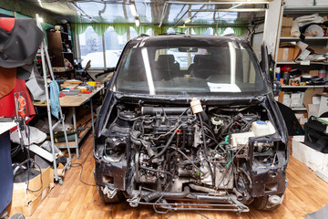 Disassembled black car in the workshop prepared for repair: front end, hood and bumper removed, internal equipment, parts and spare parts visible. Auto service industry.