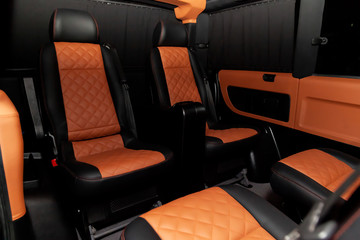 Fototapeta premium Four rear seats in a minibus are deployed to each other and tightened in black and brown leather with a diamond-shaped stitching thread in a workshop for tuning and repairing vehicles. Van car.