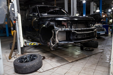 Used black car disassembled without bumper and wheels on a four-post lift for repairing the chassis and engine in a vehicle repair workshop. Auto service industry.