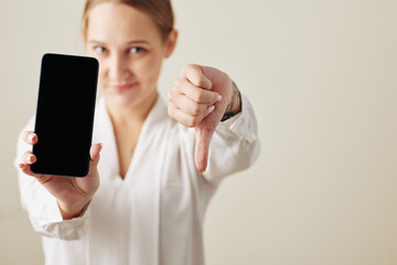 Young businesswoman with smartphone showing thumbs down, selective focus