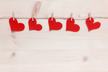 Five red textured Valentine hearts pinned to pack thread on wooden background.