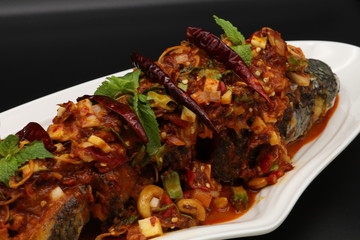 Thai spicy fried fish with herbs and chili on white plate