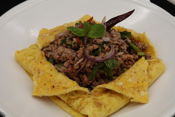 Thai minced pork cooked with chili and herbs in egg on white plate