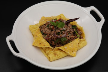 Thai minced pork cooked with chili and herbs in egg on white plate