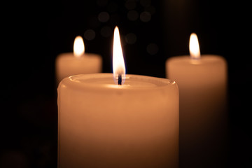  white burning candle stands before a dark background