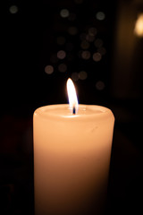  white burning candle stands before a dark background