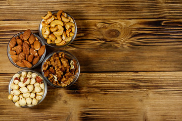 Obraz na płótnie Canvas Assortment of nuts on wooden table. Almond, hazelnut, walnut and cashew in glass bowls. Top view, copy space. Healthy eating concept