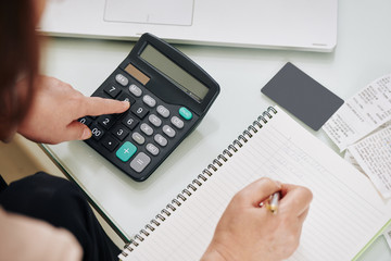 Close-up image of woman calculating expenses and incomes and writing in textbook, view from above