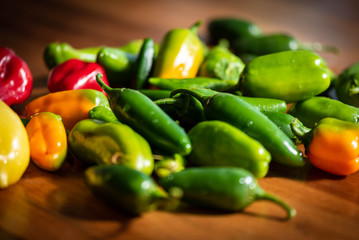 Fresh variety of green, red, orange and yellow peppers on the wooden background.