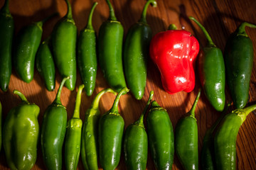 Fresh variety of many green peppers and one red pepper on the wooden background.