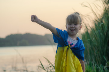 Little girl in a white dress with a yellow-blue flag of Ukraine in hands. Child in background of sky. Happy Ukrainian. Little Ukrainian with a flag. Independence day Ukraine.