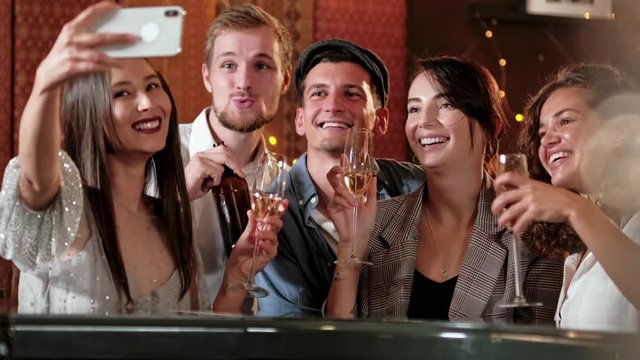 Young Cheerful Female Friends Taking Selfie In Pub Using Phone. Friends, men, women, leisure, friendship and technology concept - friends with smartphones drinking beer at bar or pub