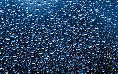Classic Blue background. Color of the year 2020. The texture of rain drops on the glass close-up. Macro transparent water drops on dark background.