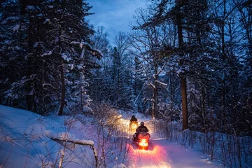 Fotobehang snowmobile in the evening goes through the winter forest. headlights. night road through the winter forest. snowmobile at night © suvorovalex