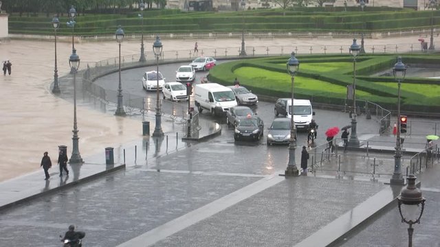 Zoom shot over a roundabout near the Louvre museum, with people crossing a street in a rainy day, Paris, France.