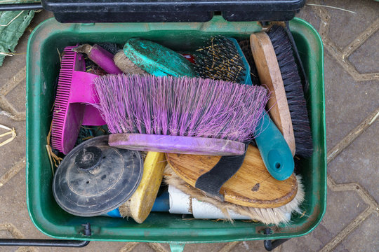 Green plastic box filled with a pile of old, colorful, worn out brushes for grooming horses - Flat lay, top down view, Horizontal format