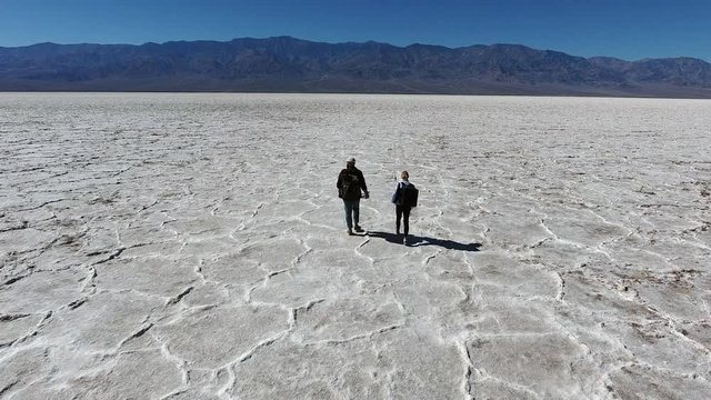 Back view of hipster guys with rucksack walking on dry surface in Badwater enjoying breathtaking environment,experienced tourists exploring wild desert lands in USA having wanderlust trip on vacations