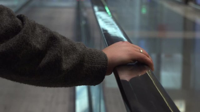 Woman with a ring standing on movable conveyor belt at the airport and holding the handrail. Person traveling to the flight on walkway escalator, travelator at international airport terminal