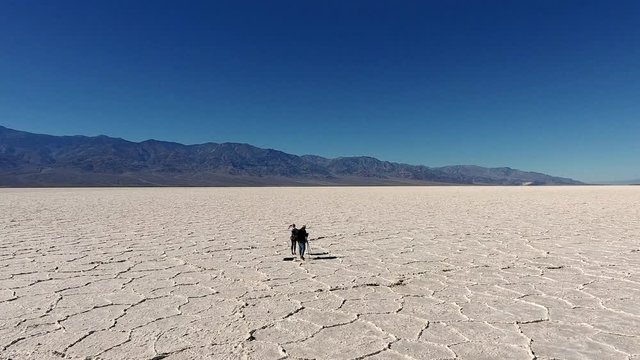 Male and female travel photographers using tripod and cellphone for shooting video of scenic locations in desert, taking photos via professional equipment while exploring Badwater basin national park
