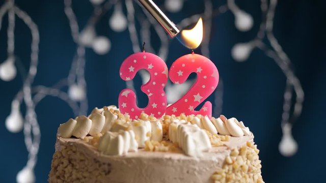Birthday cake with 32 number pink candle on blue backgraund. Candles are set on fire. Slow motion and close-up view
