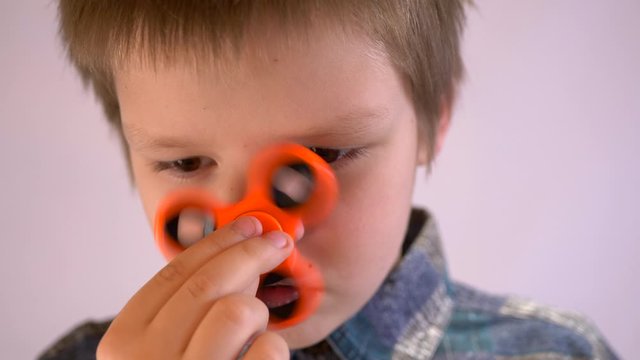 Funny blond child in striped shirt twists spinner on his nose. Portrait of boy on white background with orange spinner. 4K. Soothing toy. Autism. Exercise for preschoolers