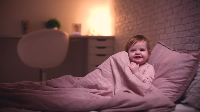 adorable little baby girl playing hide and seek in bed before going to sleep