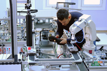 industry 4.0 concept: close-up of an engineer who is teaching robot arm the points with control panel (teach pendant) on smart factory production line. Selective Focus.