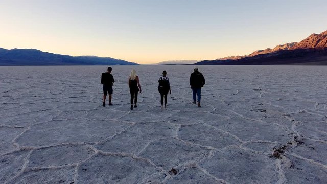 Concept of forward movement - youth people walking to their goals, scenery back view of four friends travelers walking on salt flats lake during breathtaking journey in Badwater Basin