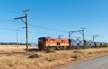 Fototapeta na wymiar Hermon, South Africa. December 2019. Freight trains hauling wagons through countryside with a mountains backdrop.