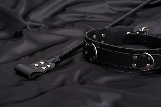 Stack for BDSM games and leather collar on black silk background