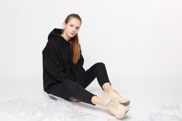 Young girl wearing blank and oversize black long hoody and balck jeans pants . Sitting on white...