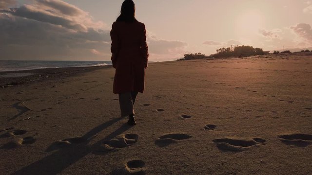 Sagoma di una ragazza che cammina sulla spiaggia al tramonto vicino l'oceano