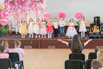 Children's party in primary school. Young children on stage in kindergarten appear in front...