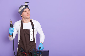 Technician being ready to solder something, attractive male wears white casual shirt, cap and brown...