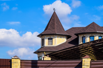 Decorative metal on the roof of a brick house. Fence made of corrugated metal.