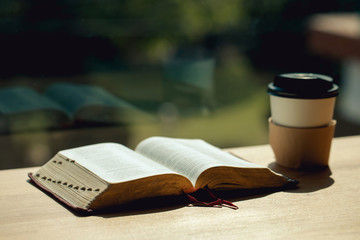 Open book with cup of coffee on wooden desk beside the window