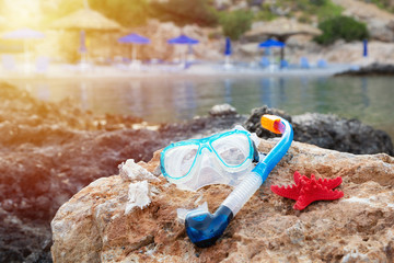 Snorkeling mask, plastic tube equipment, seashells and red starfish on the rock close sea. Blue sun umbrellas on a beach. Symbol for holiday vacation.