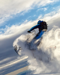 a snowmobile rider jumps in a mountain valley at dawn. sports snow bike with snow splashes and snow trail. bright snowmobile and suit without brands. snowmobilers sports riding. stock photo