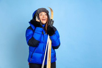 Skii lover. Caucasian woman's portrait on blue studio background. Beautiful female model in warm clothes. Concept of human emotions, facial expression, sales, ad. Winter mood, Christmas time, holidays