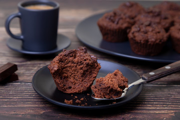 Chocolate muffins on a black plate. Homemade baking. In the background is a cup of coffee and a plate with muffins. Wooden background. Selective focus, close up.