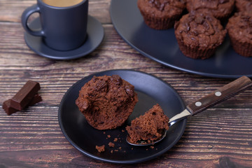 Chocolate muffins on a black plate. Homemade baking. In the background is a cup of coffee and a plate with muffins. Wooden background. Selective focus, close up.