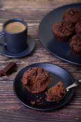 Chocolate muffins on a black plate. Homemade baking. In the background is a cup of coffee and a plate with muffins. Wooden background. Selective focus, close up.