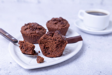 Chocolate muffins on a white plate. Homemade baking. In the background is a cup of coffee. White background. Selective focus, close up.
