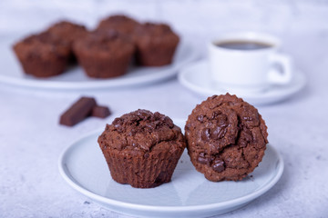 Chocolate muffins on a white plate. Homemade baking. In the background is a cup of coffee. White background. Selective focus, close up.