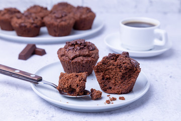 Chocolate muffins on a white plate. Homemade baking. In the background is a cup of coffee. White background. Selective focus, close up.