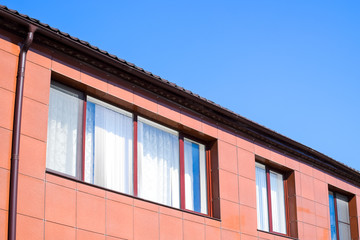 Plastic windows on the house and a spillway system on the roof. House with plastic windows and a brown roof of corrugated sheet